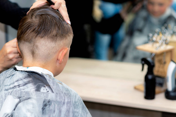 Arrière vue Gros plan caucasien américain jolie écolier garçon coiffure à la mode à lumineux salon de coiffure moderne. - Photo, image