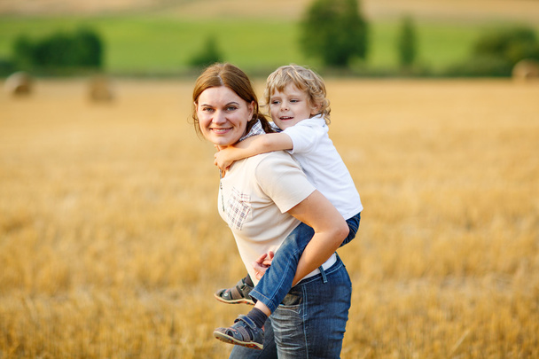 Young mother and her little son having fun on yellow hay field - Foto, Imagen