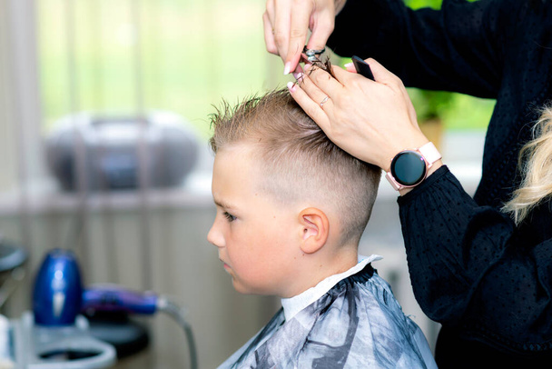 Poważny chłopiec szkolny będzie gotowy coraz modne fryzury z przeterminowanego fryzjera w modnym salonie fryzjerskim. - Zdjęcie, obraz