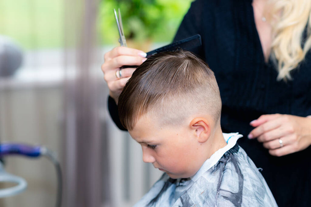 Zamknij się kaukaski amerykański ładna szkoła chłopiec czesane po fryzury w jasny nowoczesny fryzjer. - Zdjęcie, obraz