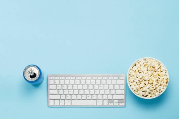 Keyboard and tin can with a drink, energy drink, a bowl of popcorn on a blue background. The concept of watching movies, TV shows, sports events online. Flat lay, top view - Photo, Image