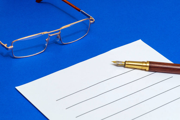 Üres dokumentum írásához tollal és szemüveggel egy kék irodai asztalon - Fotó, kép