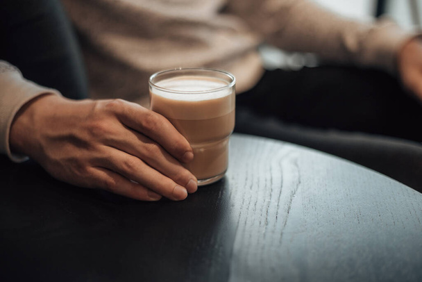 Close-up shot van de man hand te houden glas kopje hete koffie tijdens het zitten in het café. Vrijgezel kleine ondernemer ochtend routine, planning. Latte, americano, capuccino, espresso concept.   - Foto, afbeelding