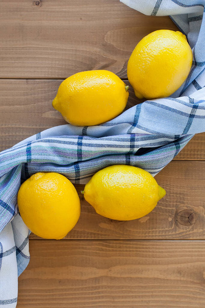 Группа из четырех целых желтых лимонов, на деревянном фоне возле полотенца в клетке. - Фото, изображение