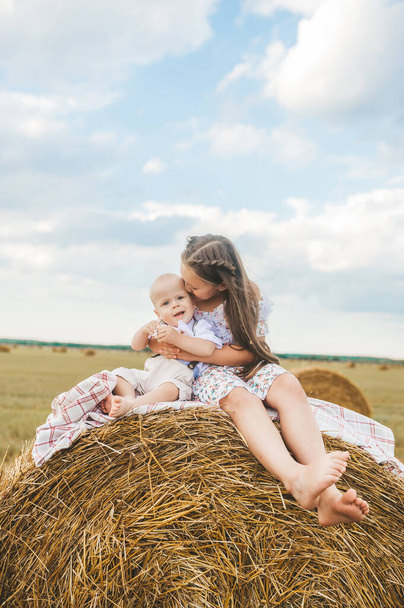 Close-up de irmã e irmão mais novo beijando no fardo de feno no campo de trigo. Menino pré-escolar e menina brincam em fardos de feno durante a época de colheita de verão na Bielorrússia - Foto, Imagem