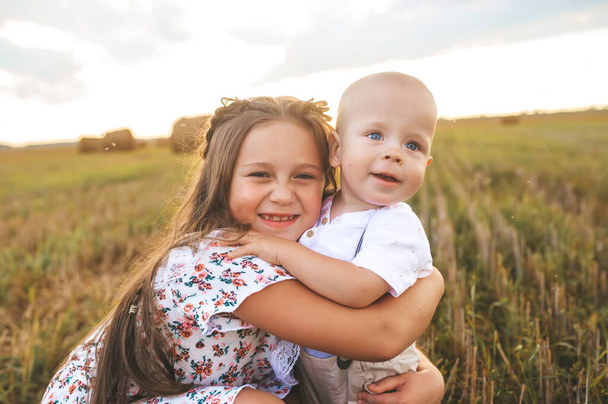 Nahaufnahme zweier Kinder, die im Weizenfeld posieren. Porträt weißrussischer Kinder bei Sonnenuntergang. Junge und Mädchen im Vorschulalter haben Spaß während der Sommererntezeit in Weißrussland. - Foto, Bild