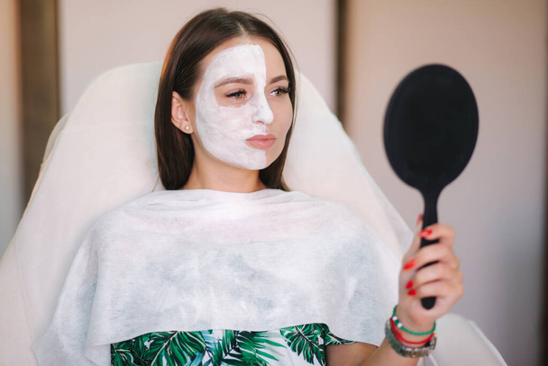 Beautiful woman with white mask on hulf of face. Attractive brunrtte woman in beauty salon - Photo, Image