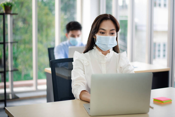 オフィスで働くウイルス保護のための医療マスクを持つアジアのビジネス人。新しい正常な社会的距離の概念は. - 写真・画像
