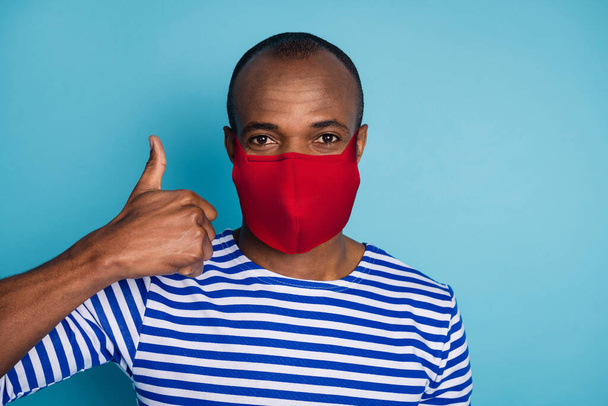 Close-up portrait of his he nice healthy guy wearing red cotton textile reusable safety mask showing thumbup stop mers cov influenza disease prevention isolated over blue color background - Photo, Image