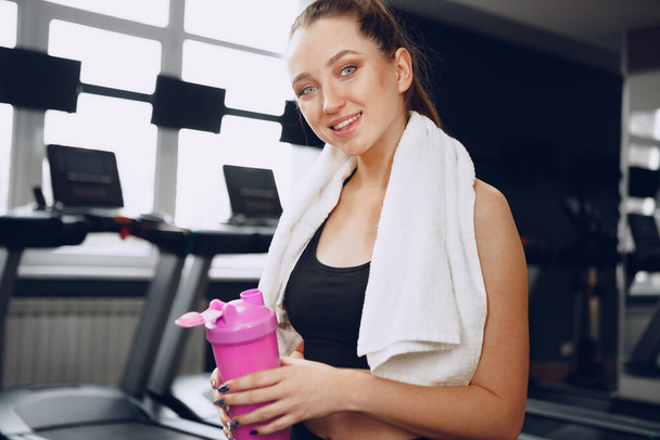 Young sporty woman having a drink in a gym after workout - 写真・画像