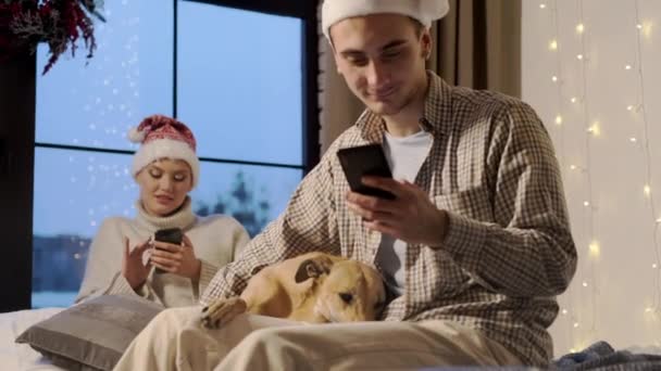 Újév. Fiatal pár télapó kalapban szilveszterkor otthon a kutyájukkal. - Felvétel, videó