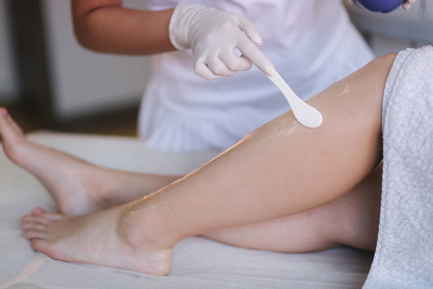 Junge Kosmetikerin mit Maske trägt Kontaktgel auf das Bein einer Frau zur Laser-Haarentfernung in der Klinik auf. Nahaufnahme - Foto, Bild