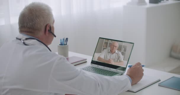 мужчина врач общается со своим пациентом в Интернете, пожилой человек говорит о симптомах и врачи пишут - Кадры, видео