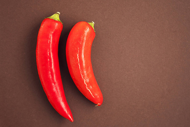 Set of two red chili peppers on the brown background - 写真・画像