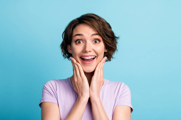 Portrait of astonished positive cheerful girl impressed wonderful bargain novelty touch face hands wear good look clothes isolated over blue color background - Foto, afbeelding