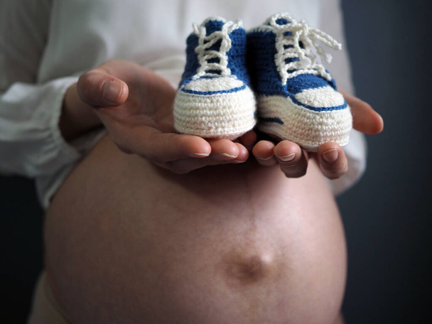 Zwangere vrouw houdt kleine baby schoenen ontspannen thuis - Foto, afbeelding