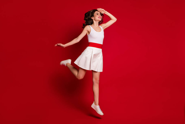 Full size profile photo of funny crazy lady jumping high up good mood rejoicing look far away hand help eyes see better wear white short dress shoes isolated red color background - 写真・画像