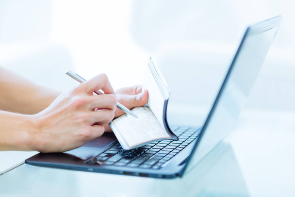 Primer plano de las manos de una persona escribiendo un cheque bancario como una transacción de dinero mientras está en línea en un ordenador portátil en el interior. - Foto, imagen