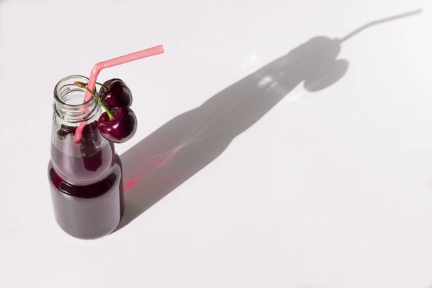 Zumo de cereza en una botella sobre fondo azul. Una bebida fresca de bayas dulces. Cereza roja madura - Foto, imagen