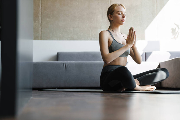 Photo of calm beautiful woman in sportswear meditating while working out in bright room - Foto, Imagen