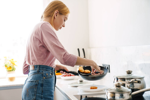 Photo of serious beautiful woman with blonde hair cooking lunch in modern kitchen at home - Fotó, kép