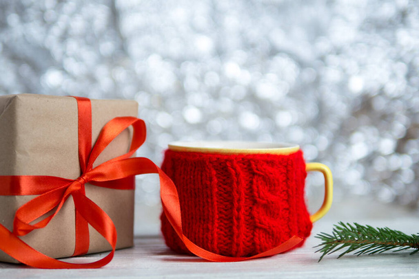 Mug in a knitted cover on a wooden white table with a Christmas gift - Photo, Image