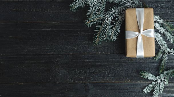 Ajándék doboz Kraft papír és fehér szalag fekete fa asztal karácsonyfa ágak - Fotó, kép