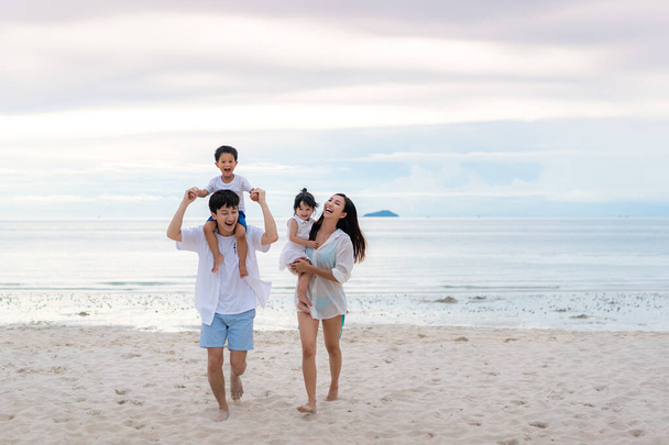楽しい父、母、息子、娘が夏の日没の海を一緒に歩いている間、幸せなアジアの家族の休日。休日、夏と休暇のビーチで幸せな家族旅行. - 写真・画像