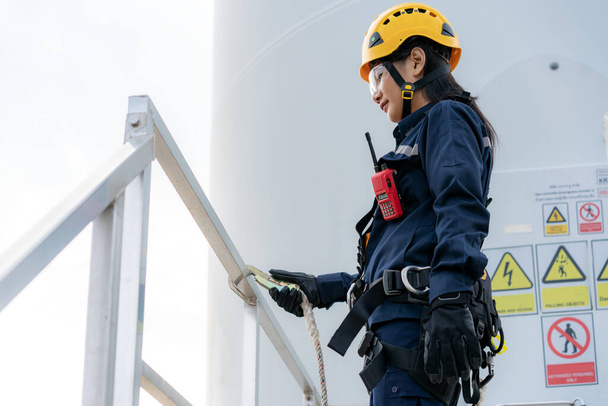 Mulher asiática Engenheira de inspeção vestindo arnês de segurança e linha de segurança trabalhando na preparação e verificação do progresso de uma turbina eólica com segurança em parques eólicos na Tailândia. - Foto, Imagem