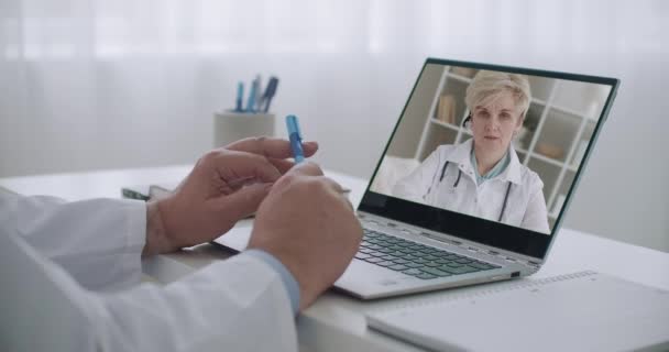 γυναίκα γιατρός συμβουλεύεται το συνάδελφό της από την ηλεκτρονική υπηρεσία, γιατρός παρακολουθεί το πρόσωπό της στην οθόνη του φορητού υπολογιστή στο γραφείο - Πλάνα, βίντεο