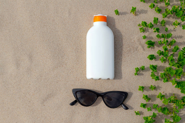 Lozione di protezione solare e occhiali da sole nella sabbia in una giornata di sole in spiaggia. Bottiglia di protezione crema solare bianca dalle scottature solari. Nessuno.. - Foto, immagini