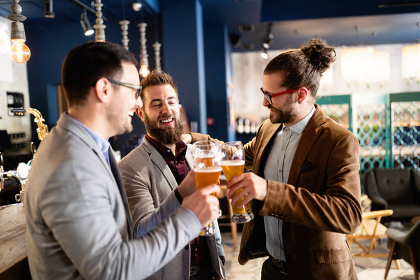 People, men, leisure, friendship and celebration concept. Happy business male friends drinking beer and clinking glasses at bar or pub - Foto, afbeelding