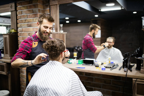 Barber shaving a bearded man in a barber shop salon - Foto, afbeelding