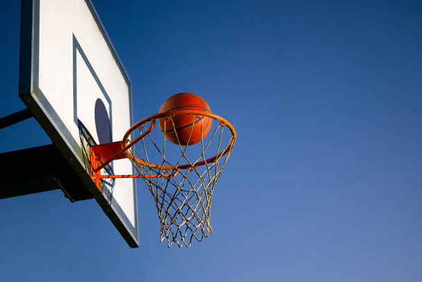 Sokak basketbolu potaya düşüyor. Arka planda mavi gökyüzü olan turuncu topu potanın üzerine yaklaştır. Başarı kavramı, sayı yapma ve kazanma. Boşluğu kopyala - Fotoğraf, Görsel