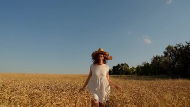 Nuori nainen kävelee onnellisena hitaasti keltaisen pellon poikki, koskettaen korvia käsillään, heiluttaen hattuaan. Kaunis huoleton nainen nauttii luonnosta. - Materiaali, video