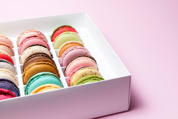 Fragment of a box with macaron or macaroon, selective focus, angled view on a pink background. Place for text. - Zdjęcie, obraz