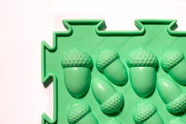 Estera ortopédica verde en forma de bellotas sobre un fondo blanco. Prevención de pies planos en niños y masaje de pies - Foto, Imagen