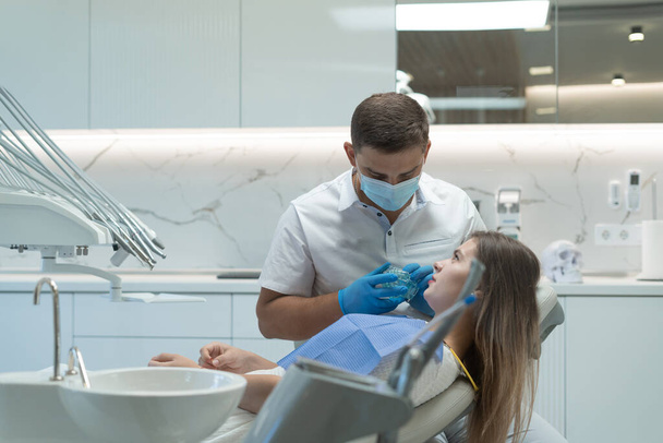 Uma bela jovem a fazer tratamento dentário no consultório do dentista. Doutor a mostrar o maxilar. Conceito de dentes saudáveis. - Foto, Imagem