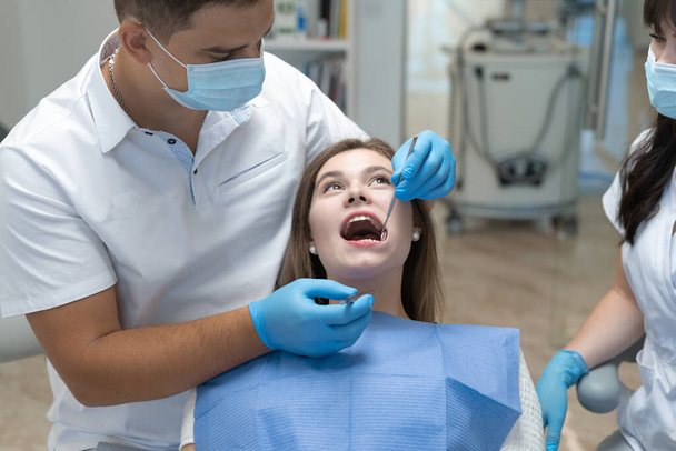 Ελκυστική νεαρή γυναίκα σε οδοντιατρική κλινική με άντρα οδοντίατρο. εξέταση της γνάθου για τερηδόνα. Υγιής έννοια των δοντιών. - Φωτογραφία, εικόνα