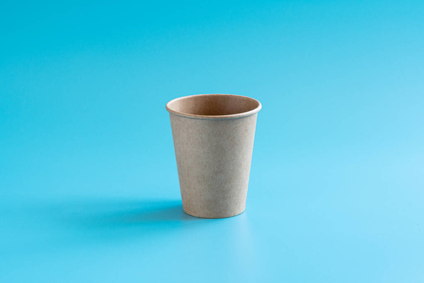 Um copo de papel artesanal marrom descartável no fundo azul. Louça ecológica. Estilo mínimo. Conceito de reciclagem e de resíduo zero - Foto, Imagem