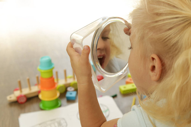 Маленька дівчинка тримає дзеркало і робить вираз обличчя
 - Фото, зображення