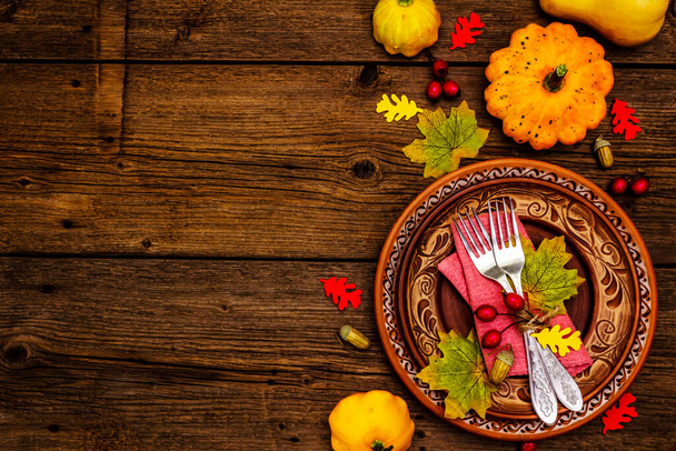 Dîner d'automne et de Thanksgiving. Récolte de citrouilles et de baies, feuilles colorées, assiettes en céramique, fourchettes et serviettes. Couverts d'automne fond en bois, vue de dessus - Photo, image