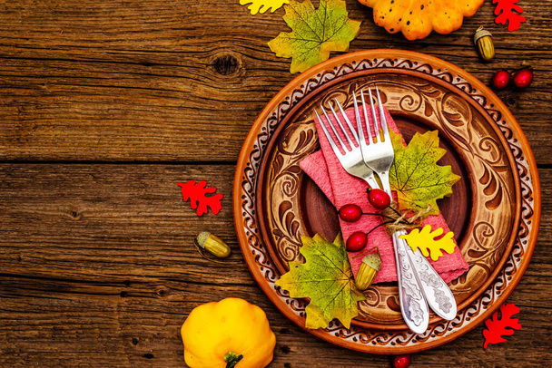 Autumn and Thanksgiving dinner place setting. Harvest of pumpkins and berries, colorful leaves, ceramic plates, forks and napkin. Fall cutlery wooden background, top view - Photo, Image