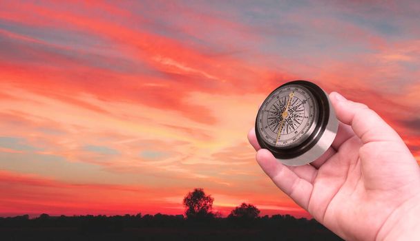 Stary klasyczny kompas nawigacyjny w ręku na tle nieba o zachodzie słońca jako symbol turystyki z kompasem, podróży z kompasem i działań na świeżym powietrzu z kompasem - Zdjęcie, obraz