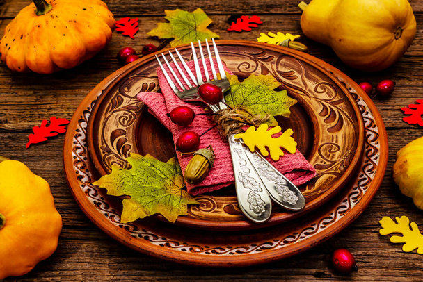 Autumn and Thanksgiving dinner place setting. Harvest of pumpkins and berries, colorful leaves, ceramic plates, forks and napkin. Fall cutlery wooden background, close up - Photo, image