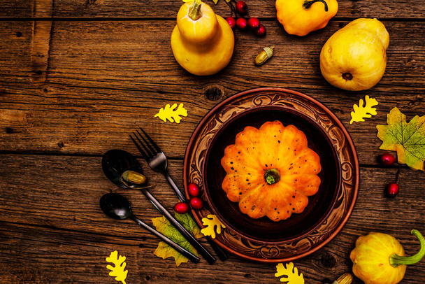 Dîner d'automne et de Thanksgiving. Récolte de citrouilles et de baies, feuilles colorées, assiette et bol en céramique, fourchette, cuillères et glands. Couverts d'automne fond en bois, vue de dessus - Photo, image