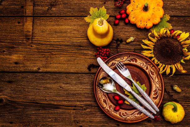 Syksyn ja kiitospäivän päivällispaikka. Sadonkorjuu kurpitsat ja marjat, värikäs lehdet, keraamiset lautaset, haarukka, lusikka, ja veitsi. Fall ruokailuvälineet puinen tausta, ylhäältä - Valokuva, kuva