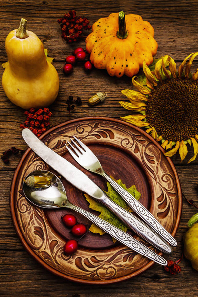 Őszi és hálaadási vacsora beállítás. Tökök és bogyók betakarítása, színes levelek, kerámia tányérok, villa, kanál és kés. Őszi evőeszközök fa háttér, közelről - Fotó, kép