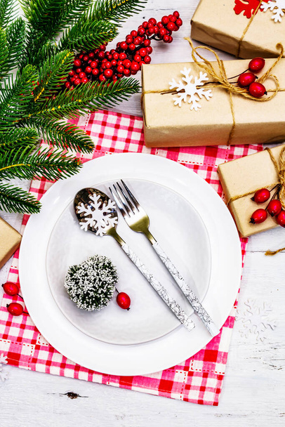 Boże Narodzenie lub Nowy Rok zero marnowania obiadu ustawienie miejsca. Płyty ceramiczne, prezent, płatki śniegu, jagody briar i tematyczne wystrój. Sztućce świąteczne na białym tle drewnianych desek, zbliżenie - Zdjęcie, obraz