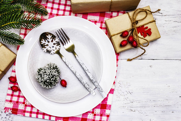 Christmas or New Year zero waste dinner place setting. Ceramic plates, gift, snowflakes, briar berries and thematic decor. Festive cutlery on white wooden boards background, top view - Photo, Image